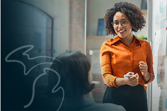 Smiling business professional standing confidently at a whiteboard with marker in hand while engaging a coworker.